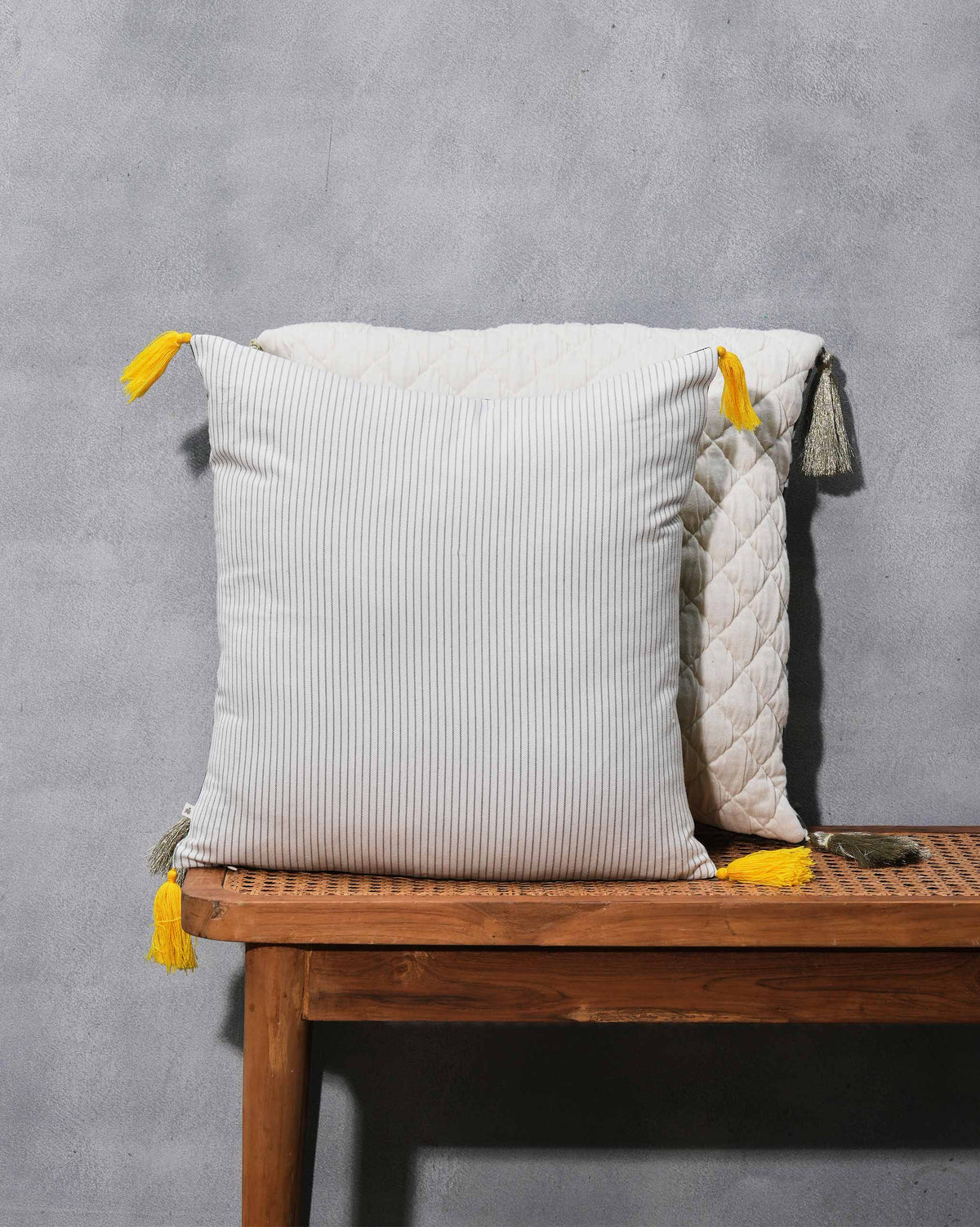 Cream pinstriped cushion with yellow tassels, in front of a quilted cushion.