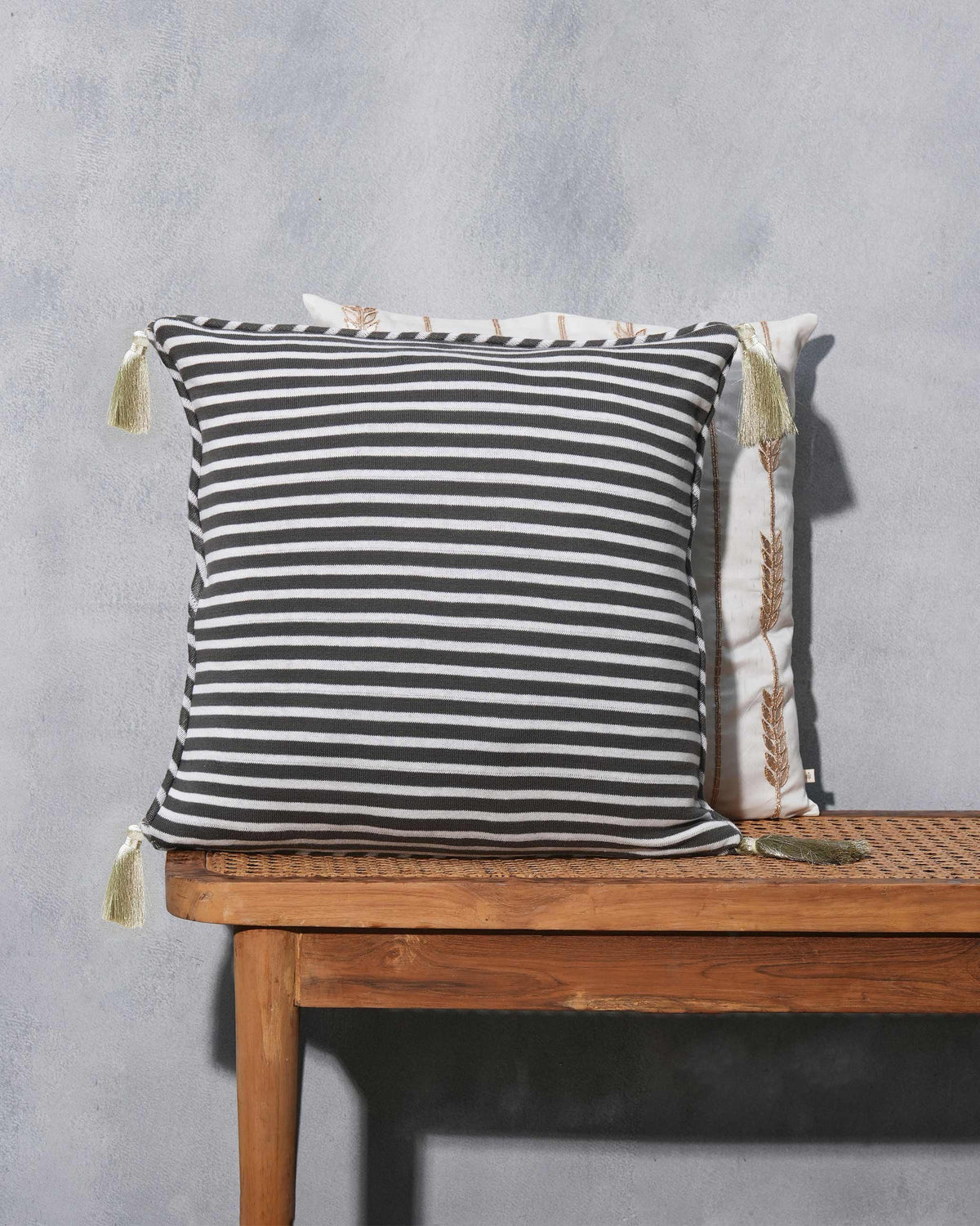 Charcoal and cream striped cushion with light olive tassels on a cane bench.