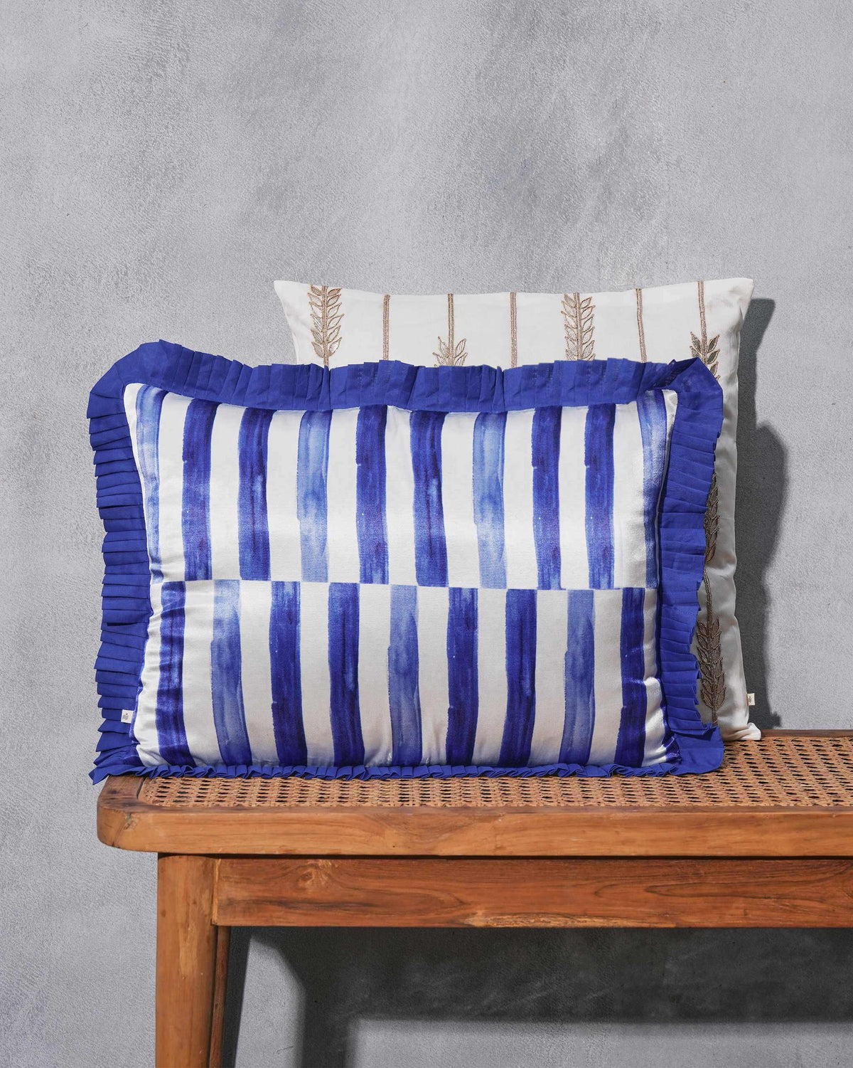 Blue striped cushion with a pleated ruffle edge on a cane bench.