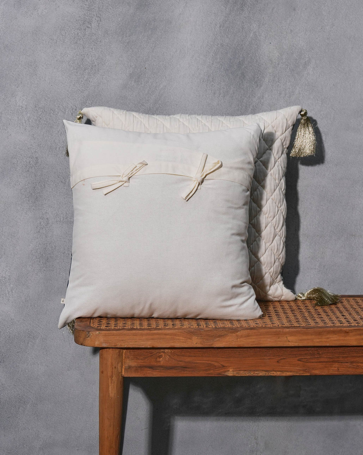 Cream cushion cover with bow ties, on a wooden bench.