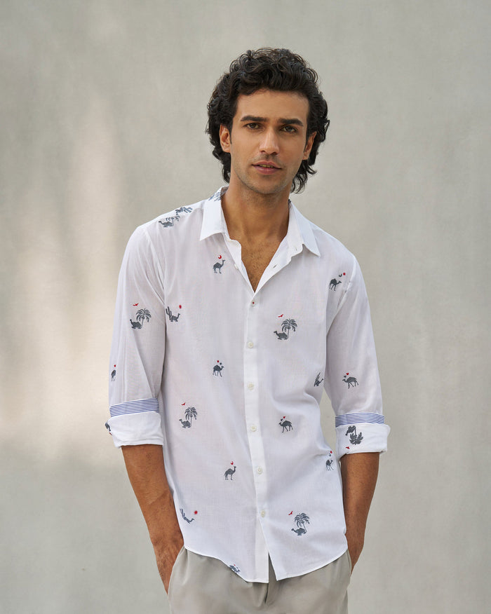 Person wearing a white Hakuna shirt with camel motifs and striped cuff lining.