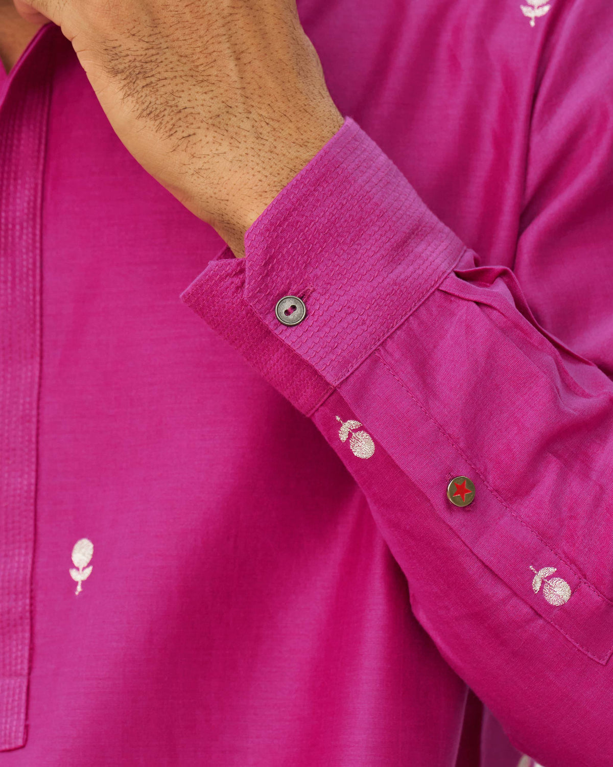 Close-up of a magenta neckband kurta sleeve with embroidered motifs at the cuff.