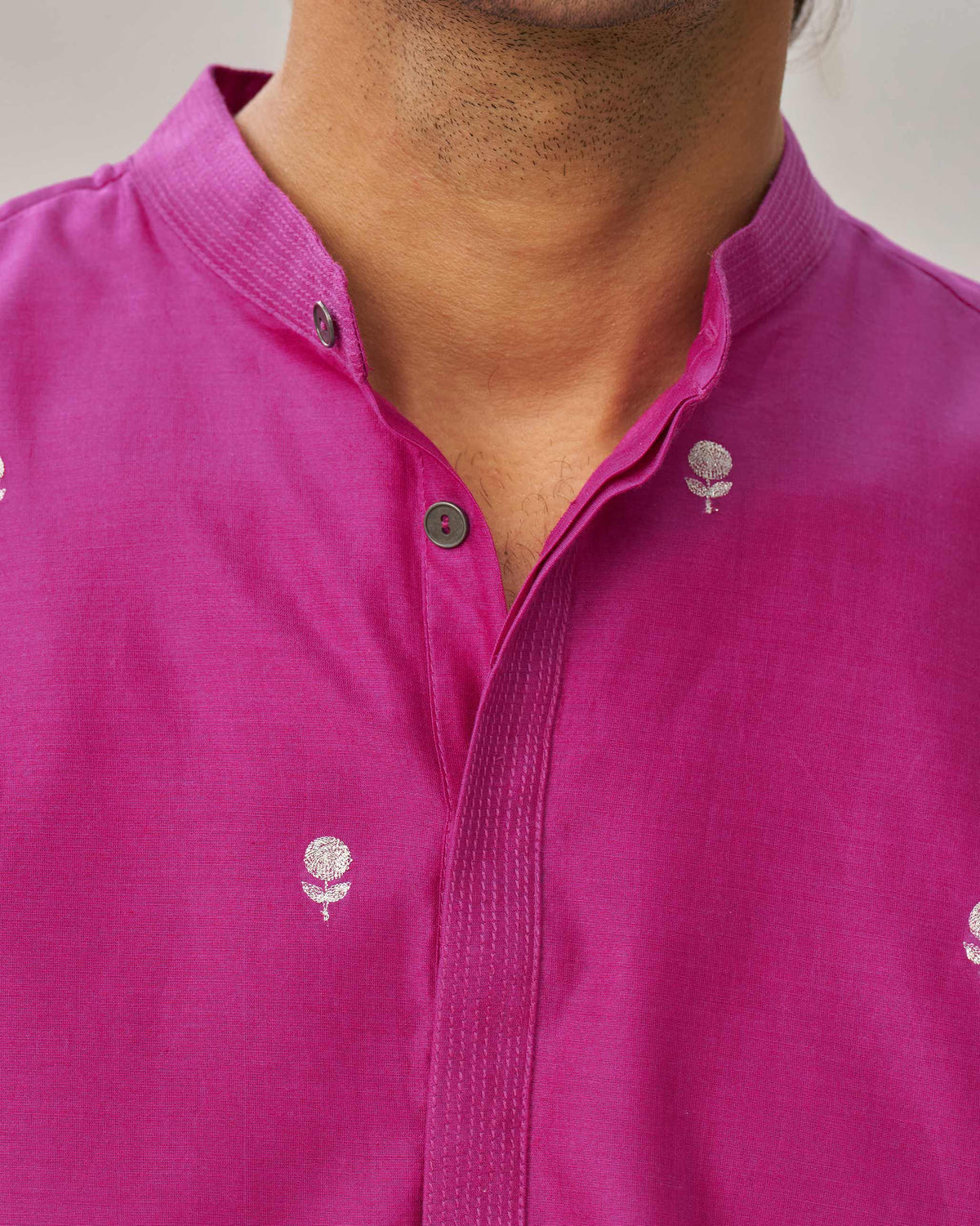 Close-up of a magenta neckband collar showing the stitched placket and embroidered motifs.