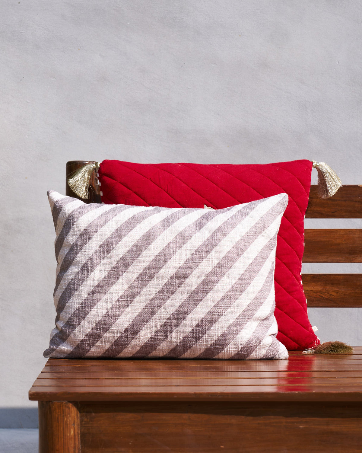 Grey and cream diagonal striped lumbar cushion cover in front of a red quilted cushion.