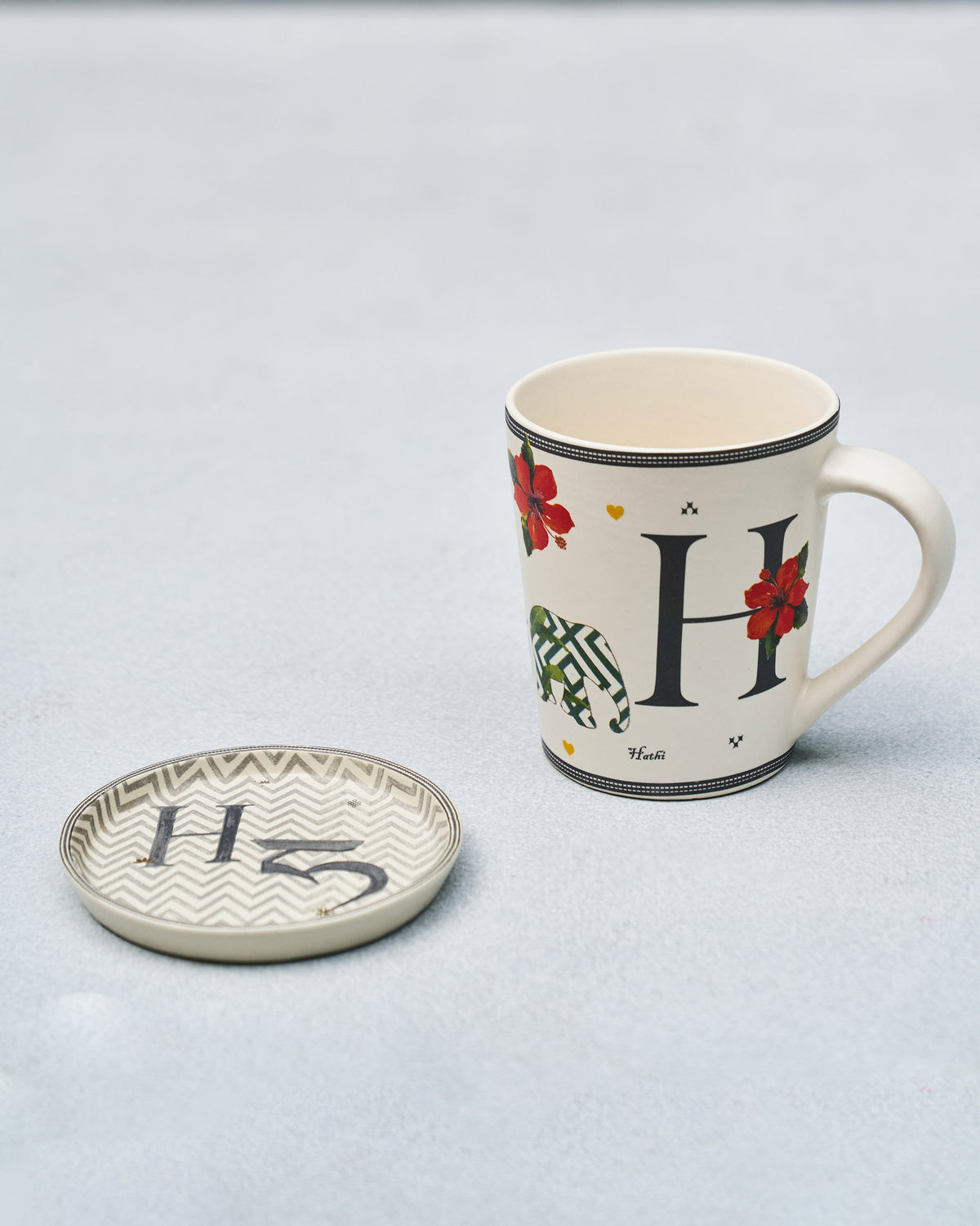 H Alphabet mug with hathi elephant and hibiscus beside a matching coaster.