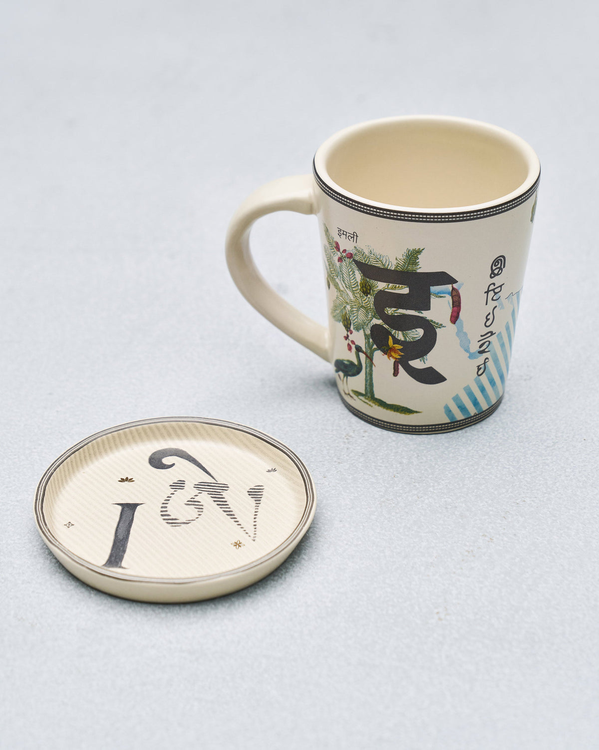 I alphabet mug with Devanagari letter and tamarind motif beside coaster.