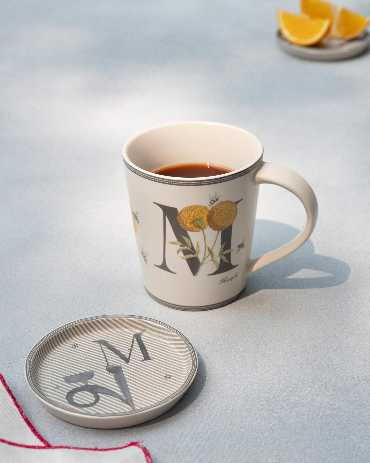 Cream M alphabet mug with coffee beside a matching coaster.