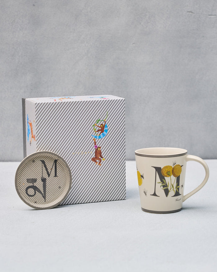 M alphabet mug with marigolds and bees beside matching coaster and gift box.