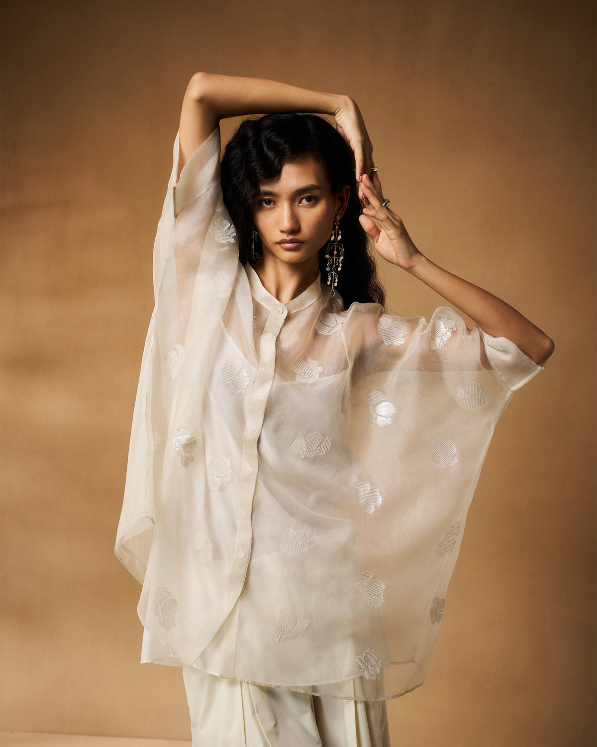 Person wearing an ivory Afra shirt with wide sheer sleeves raised.