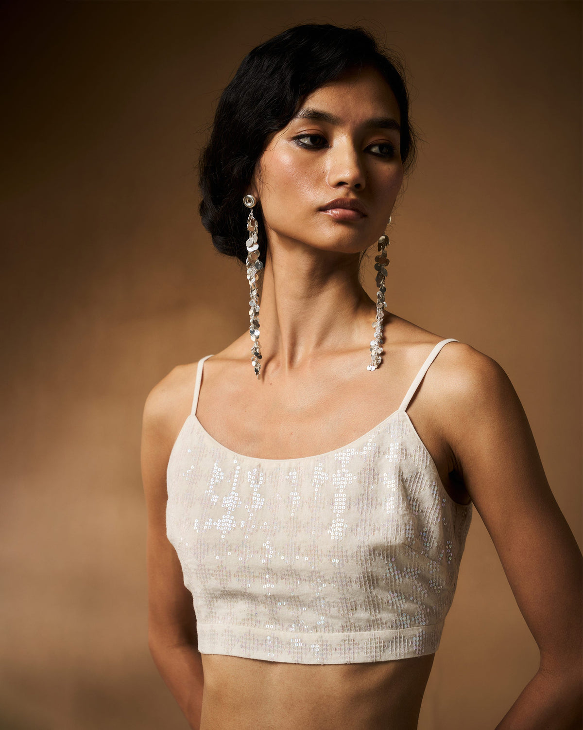 Person wearing an ivory sequined strappy cropped blouse.