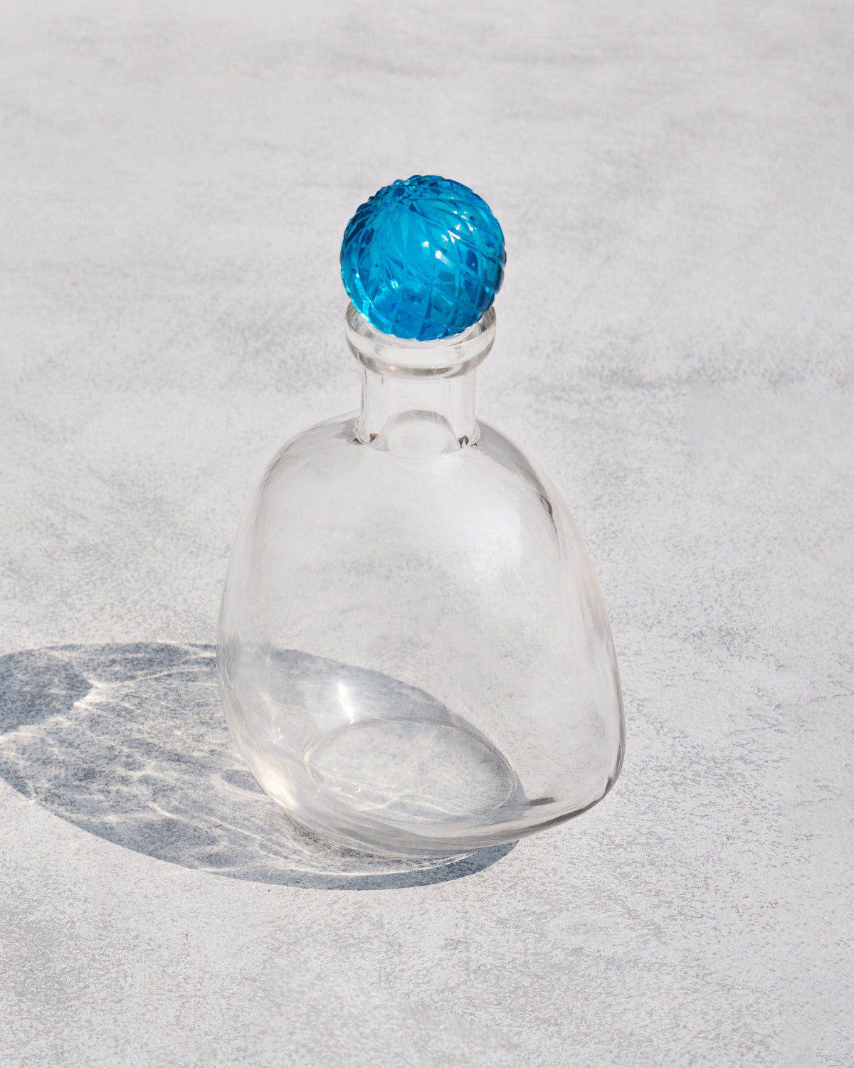 Angled view of a clear Revel Decanter with a faceted blue stopper.