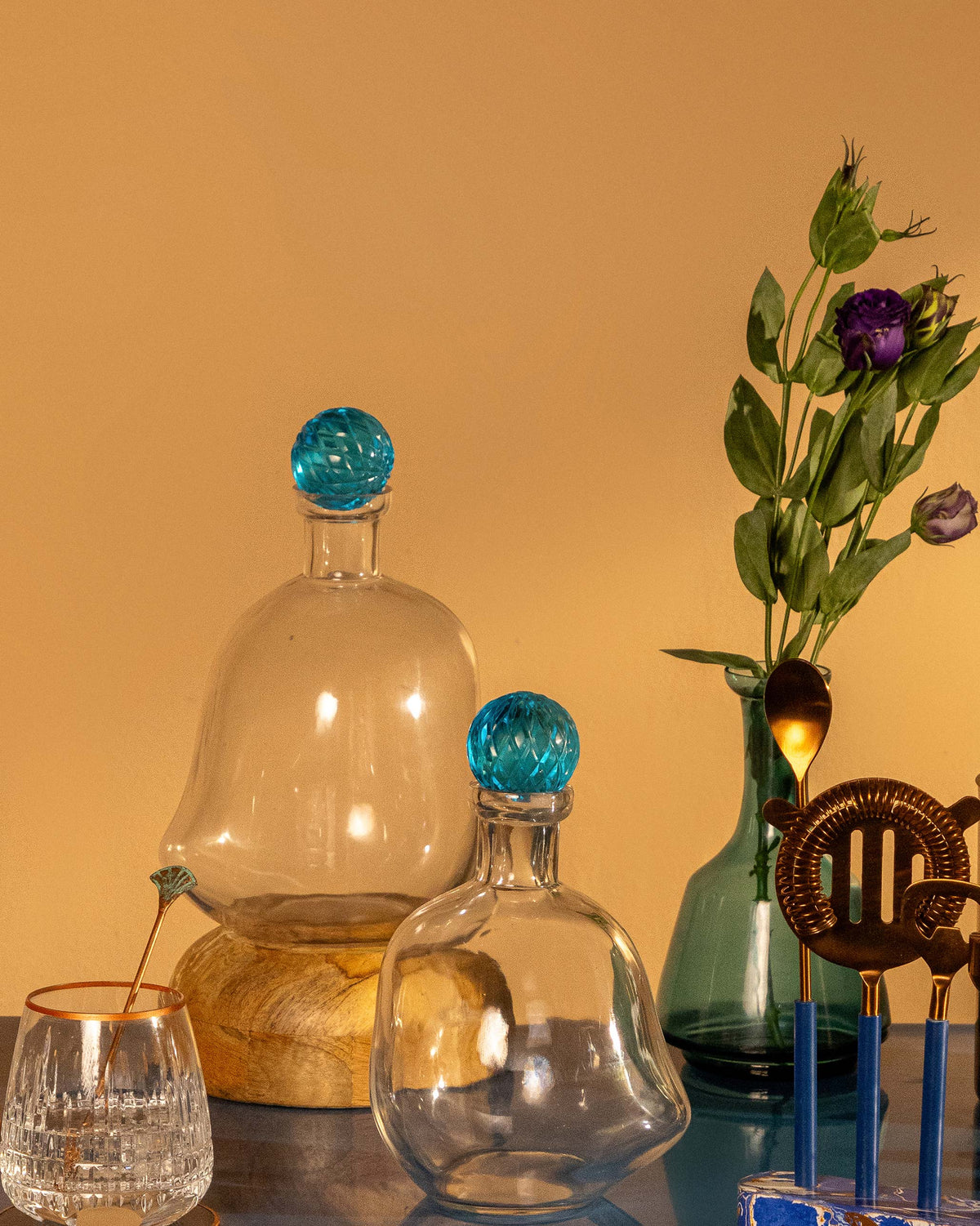 Two Large Revel Decanters with blue stoppers, one on a wooden stand.