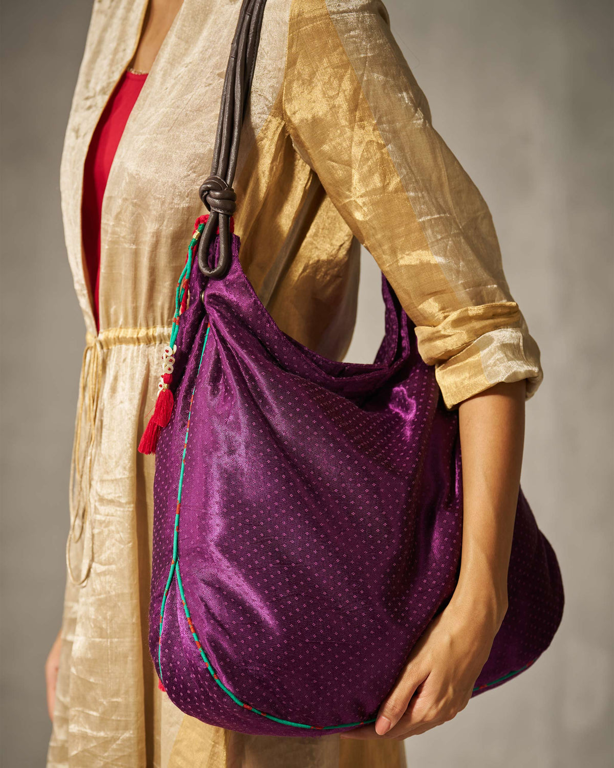 Side view of a purple Nomad Tote held at the hip, with green piping along the base.