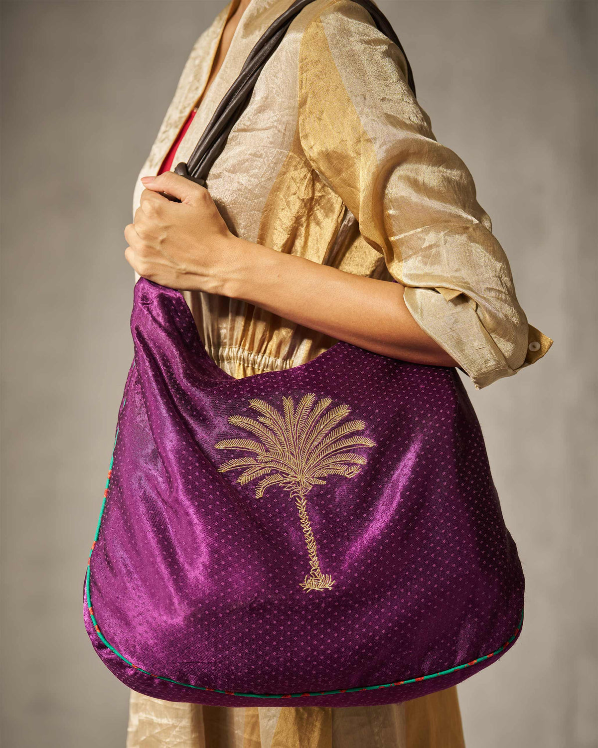 Person carrying a purple Nomad Tote on the shoulder, with its palm tree embroidery.