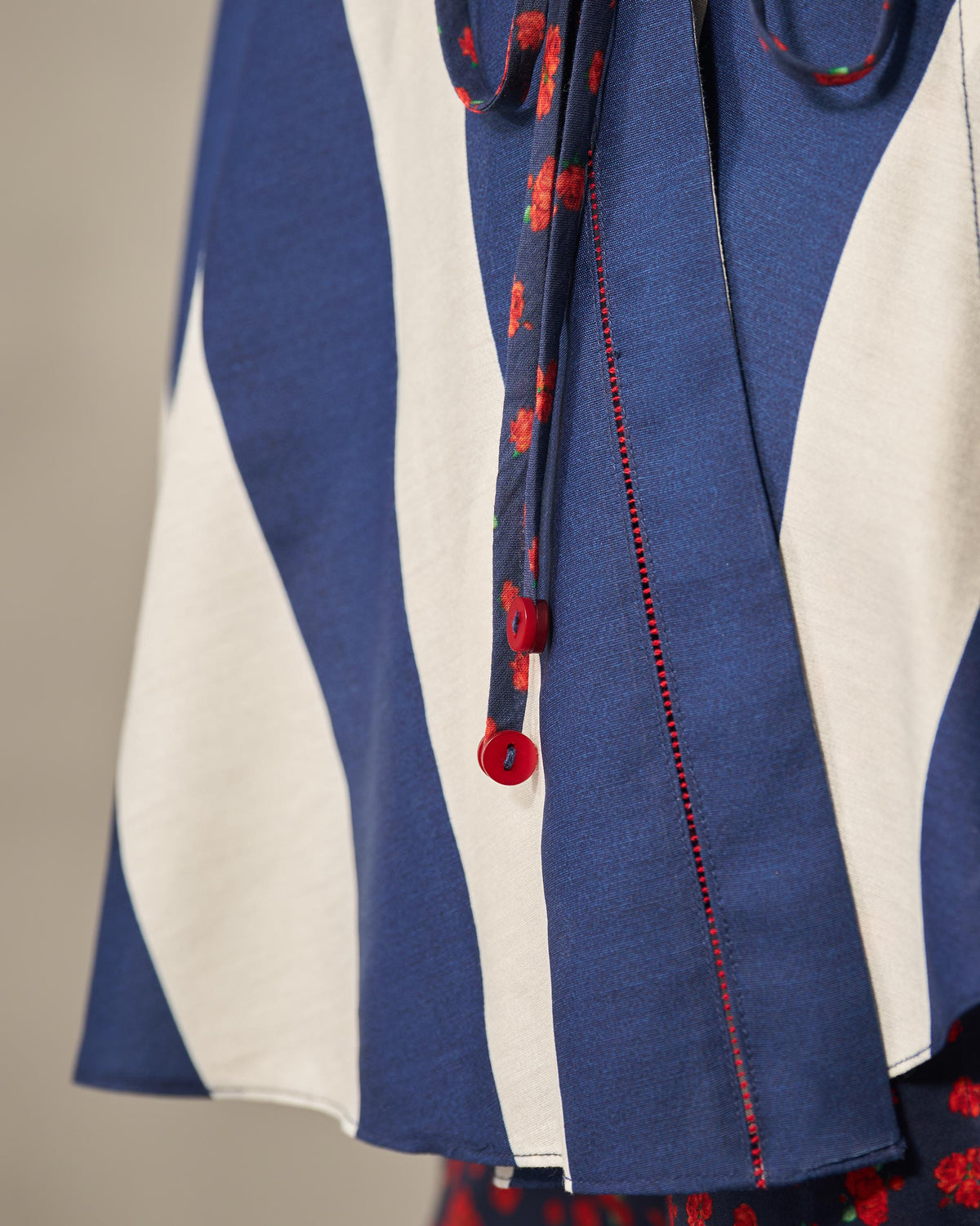 Close-up of a navy and ivory striped Fern wrap top showing a red floral tie with a red button.