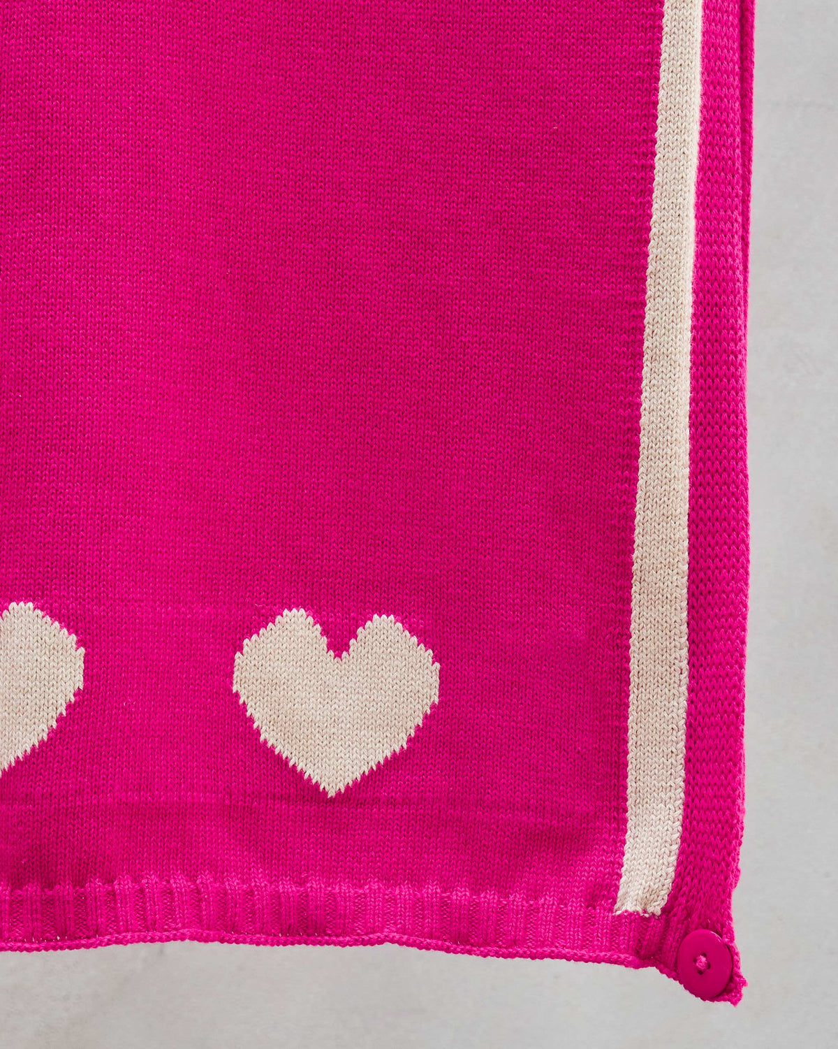 Close-up of Baby Hearts Scarf in fuchsia knit with cream hearts and an edge stripe.