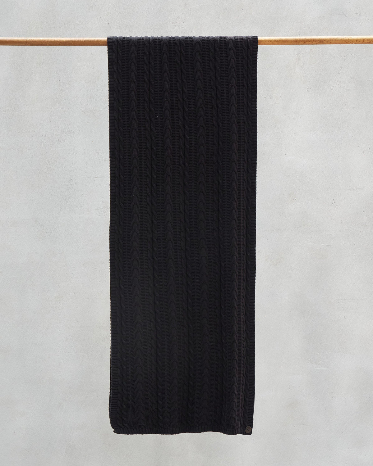 Black Pippa Scarf hanging from a wooden rail, showing its cable knit.