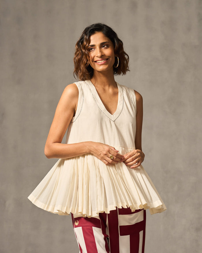 Person wearing an ivory Lolo pleated top with a V-neck and pleated hem.