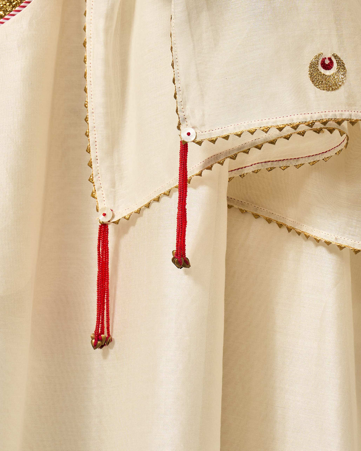 Close-up of an ivory Tangier Dupatta showing gold scalloped edging and red tassels.