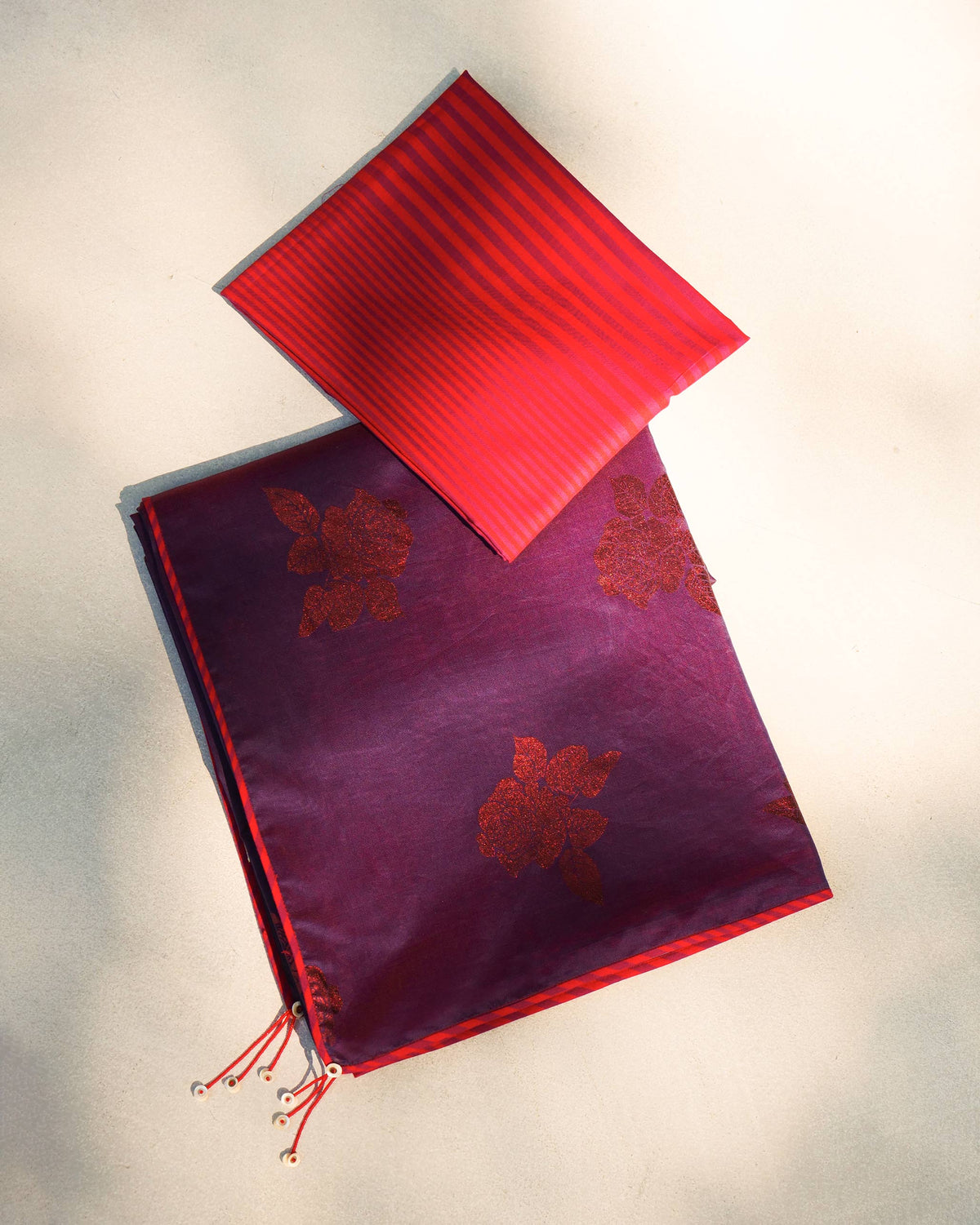 Rose Rush Sari folded flat in purple beside a red striped fabric piece.