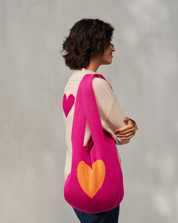 Person carrying a fuchsia Knitted Heart Bag over the shoulder, with an orange heart.