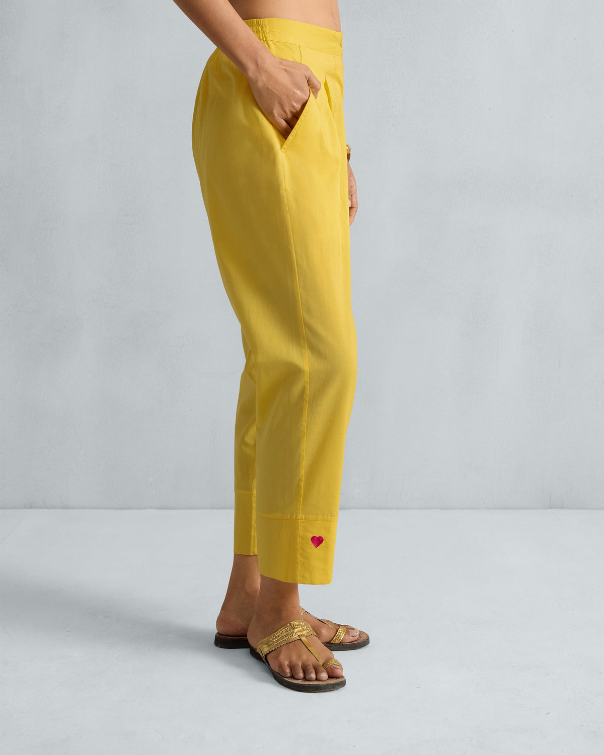 Side view of yellow Narrow pants with a pocket and a red heart at the hem.