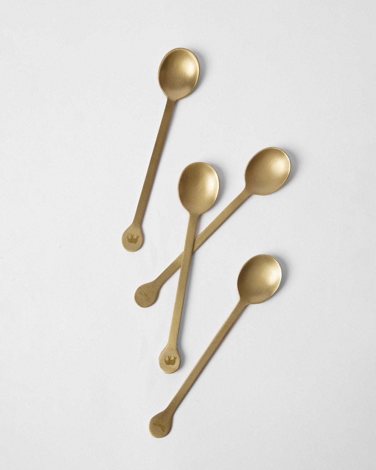 Four gold Cairo coffee spoons scattered on a white surface.