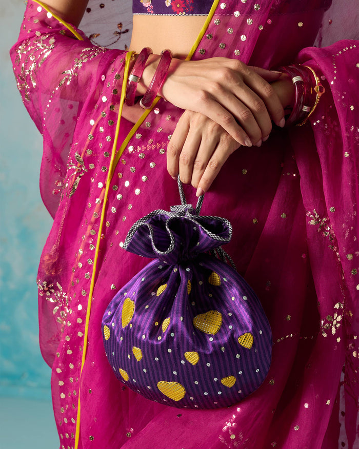 Person holding a violet Meher Potli with gold heart motifs and sequins.