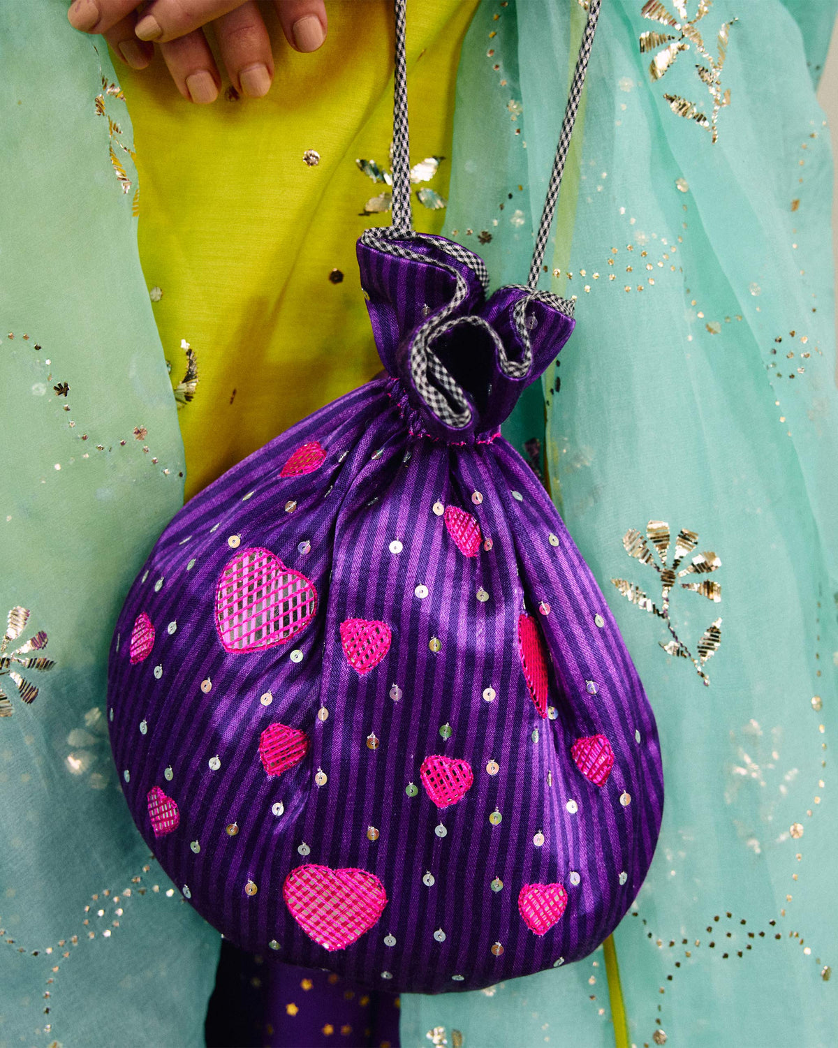 Person holding a violet Meher Potli with pink heart motifs.