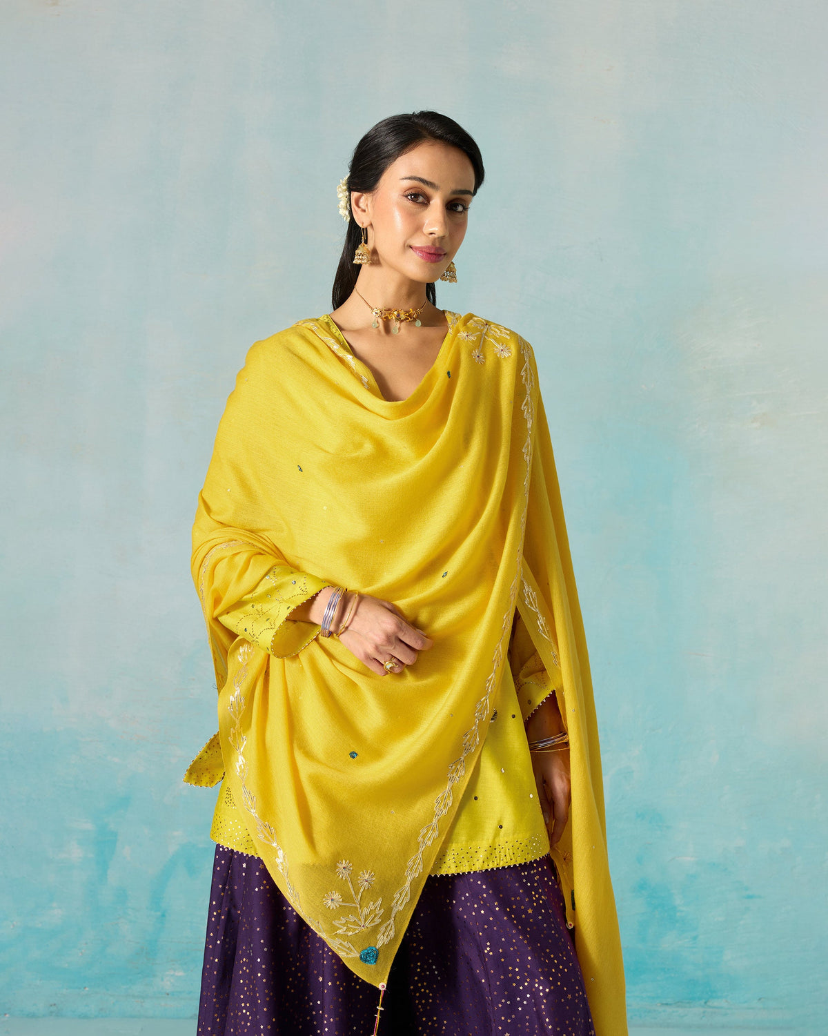 Person standing with a yellow Saanjh shawl draped over the shoulders.