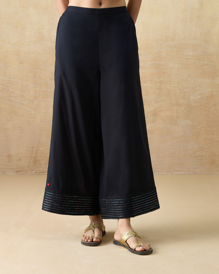 Person wearing black A-line pants with a rainbow sequin hem and red heart.