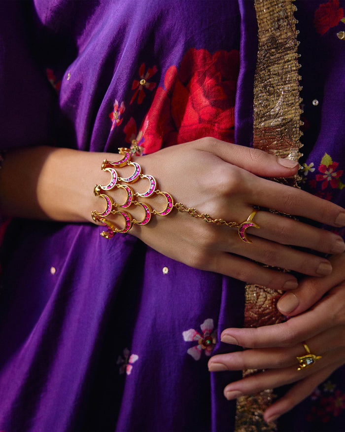 Person wearing a gold Gul Haathphool with pink crescent motifs on the hand.