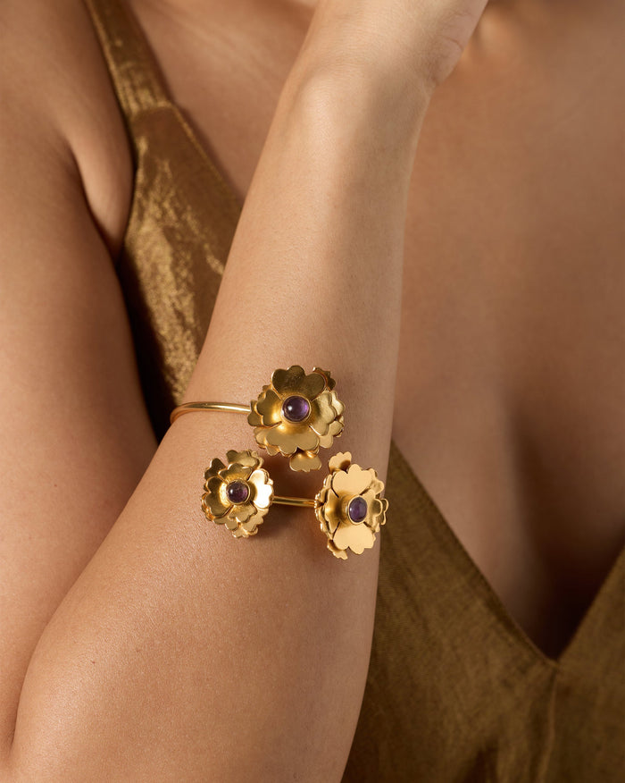 Person wearing a Kesar Phool Cuff with three gold flowers and purple stone centres.