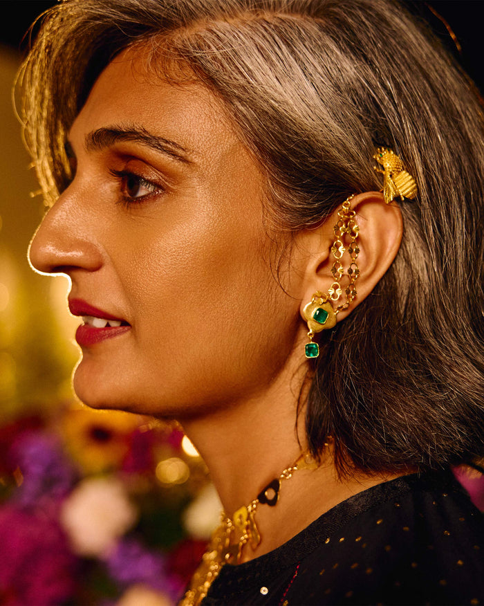 Close-up of a gold Clover Kanauti earring with green stones worn on the ear.