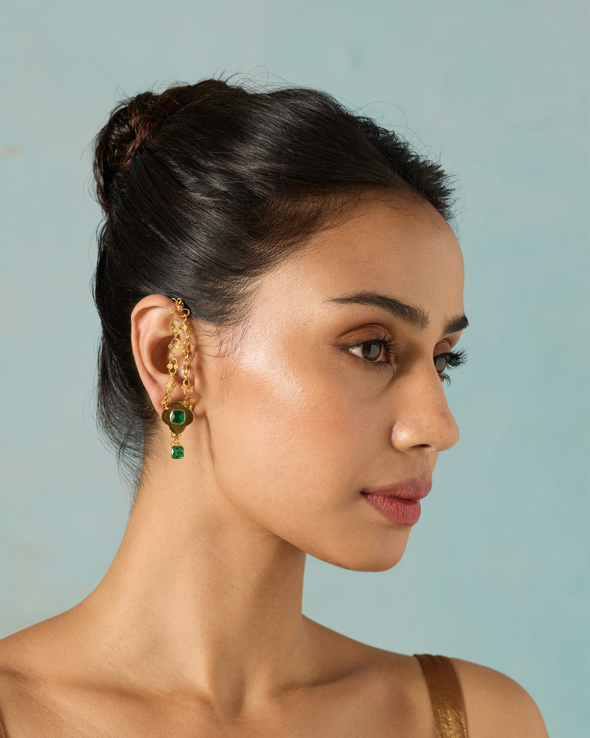 Side profile of a gold Clover Kanauti earring with green stones on a person.