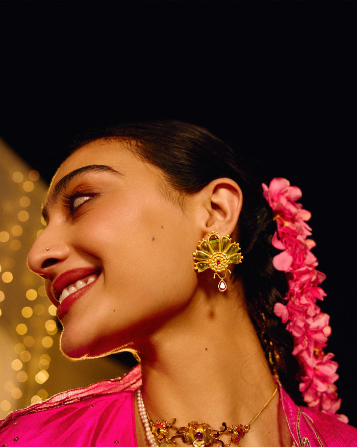 Person wearing a gold Mari-Palm earring with green petals and a pink drop.