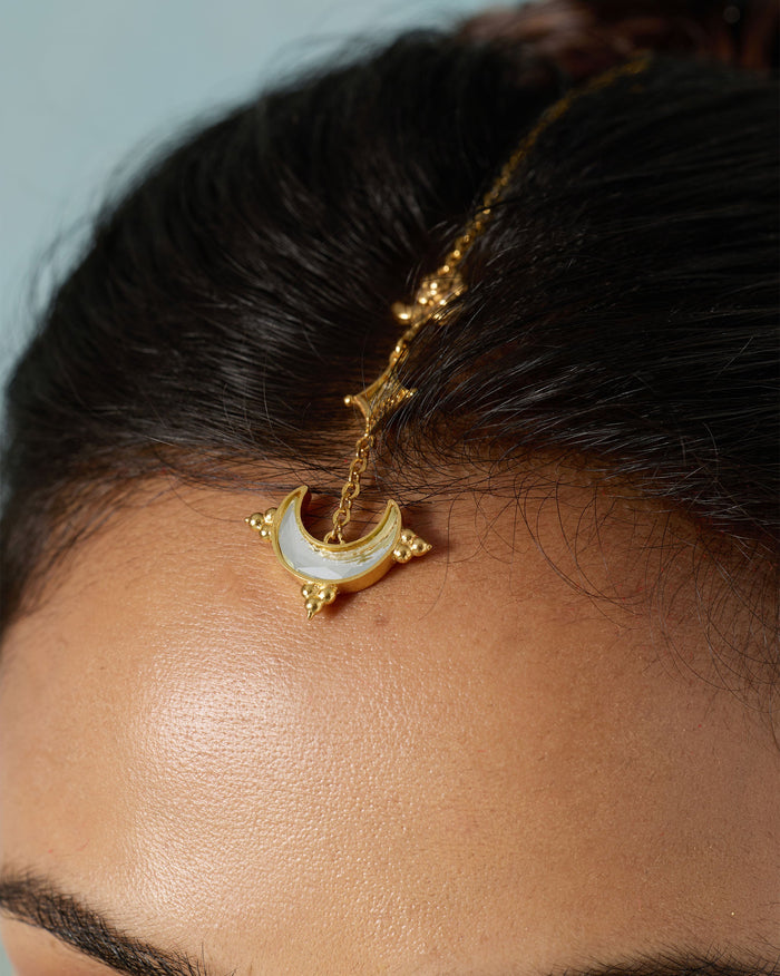 Close-up of a gold Chand maangtika with a crescent mirror pendant on a forehead.