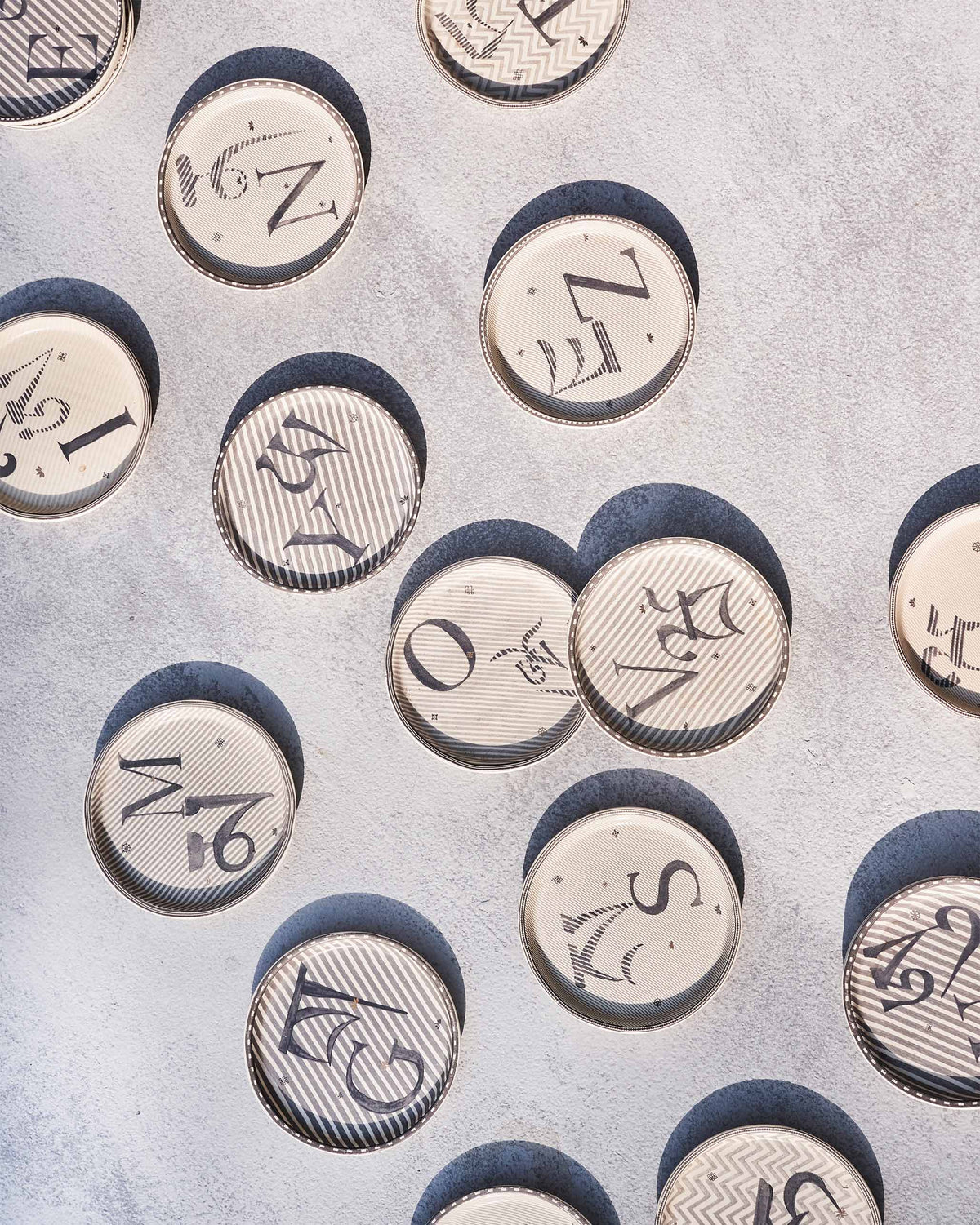 Scattered Akshar coasters with different letters on a grey surface.