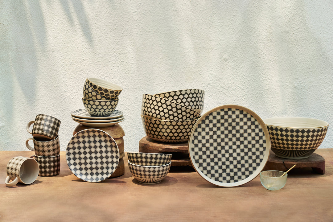 Assorted Fez dinnerware with charcoal diamond patterns stacked on wood.