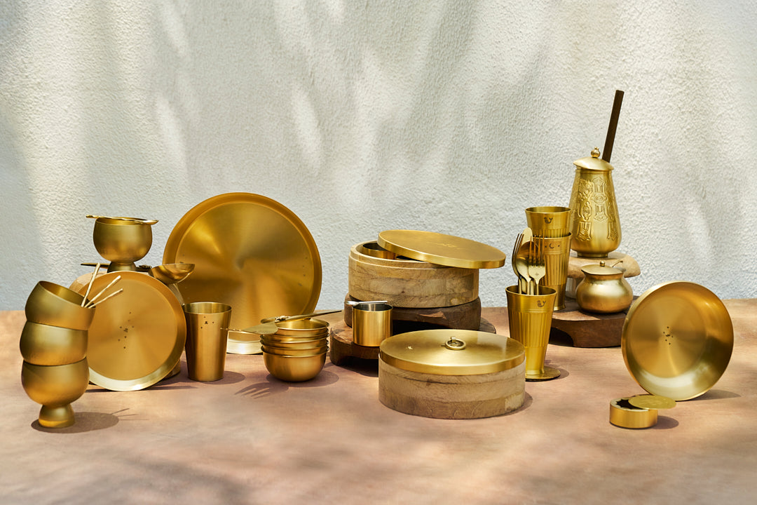 Gold tableware collection arranged on a sunlit table.